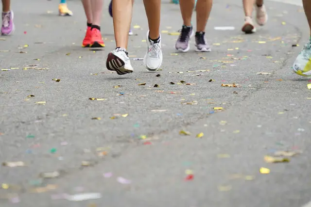 Runners in colorful shoes on a road race course scattered with confetti