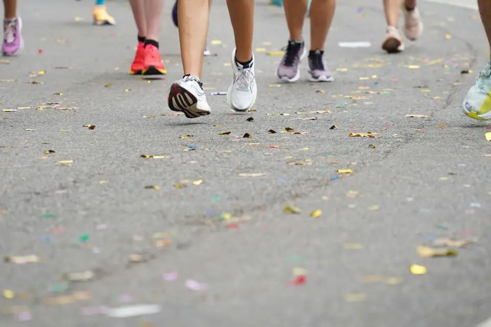 Runners in colorful shoes on a road race course scattered with confetti