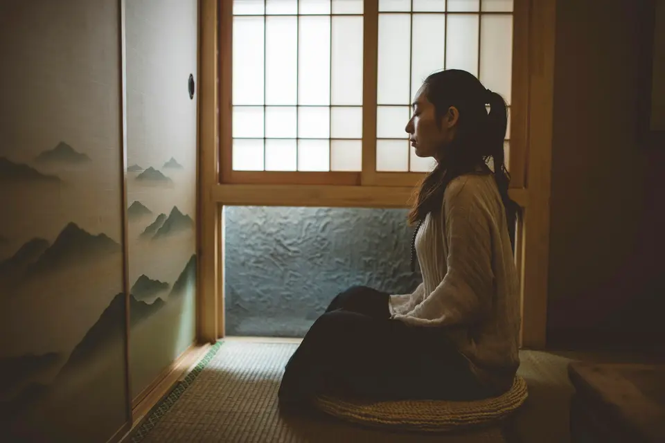 Woman sitting quietly with her eyes closed beside a bright window