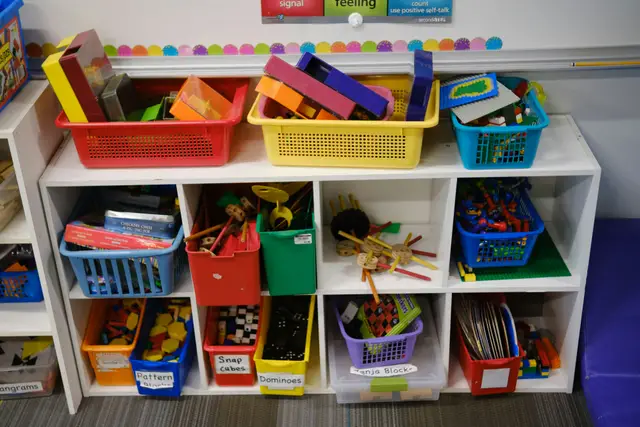Colorful storage bins filled with learning toys on white classroom shelves