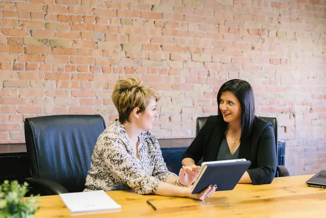 Two colleagues reviewing figures on a tablet at a wooden meeting table