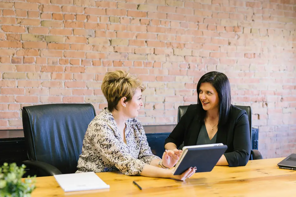 Two colleagues reviewing figures on a tablet at a wooden meeting table