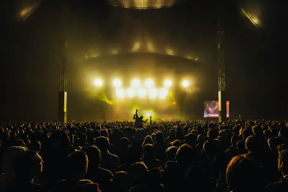Crowd facing a brightly lit concert stage with a large lighting rig