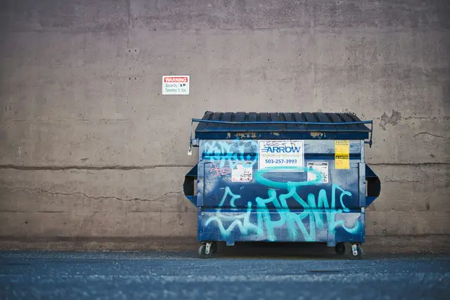 Commercial dumpster against a concrete wall behind a building