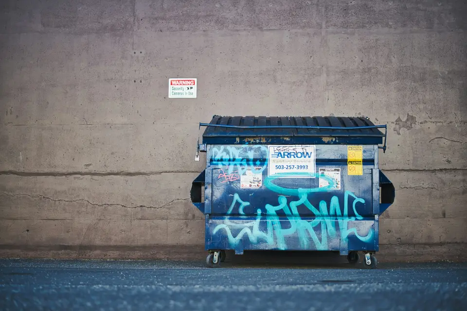 Commercial dumpster against a concrete wall behind a building