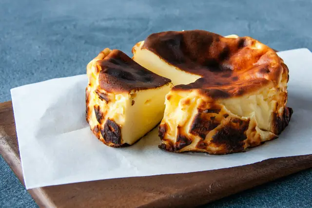 Whole Basque cheesecake with a dark caramelized top, one slice cut, on parchment paper