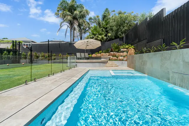 Backyard swimming pool behind a glass safety fence, with a lawn and palm trees