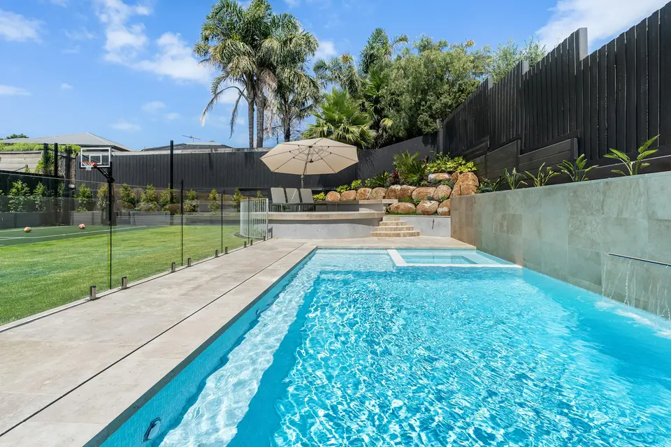 Backyard swimming pool behind a glass safety fence, with a lawn and palm trees