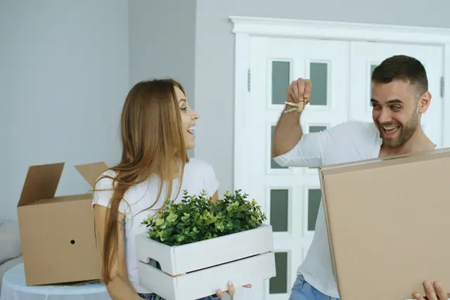 Happy couple carrying moving boxes and a plant into their new home
