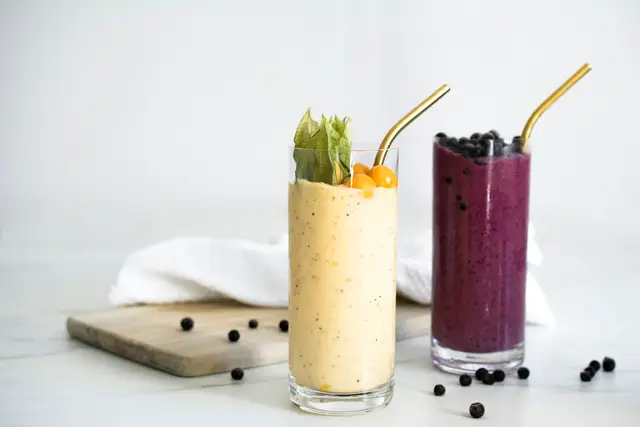 Mango smoothie and blueberry smoothie in tall glasses with metal straws on a white table