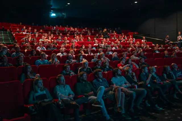 Full movie theater audience in red seats watching the screen