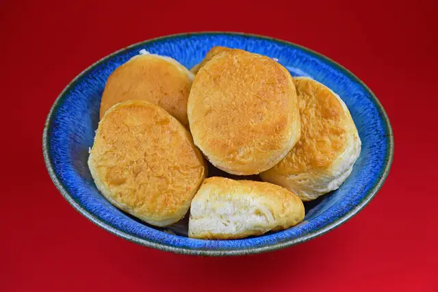 Golden buttermilk biscuits piled in a blue bowl on a red table