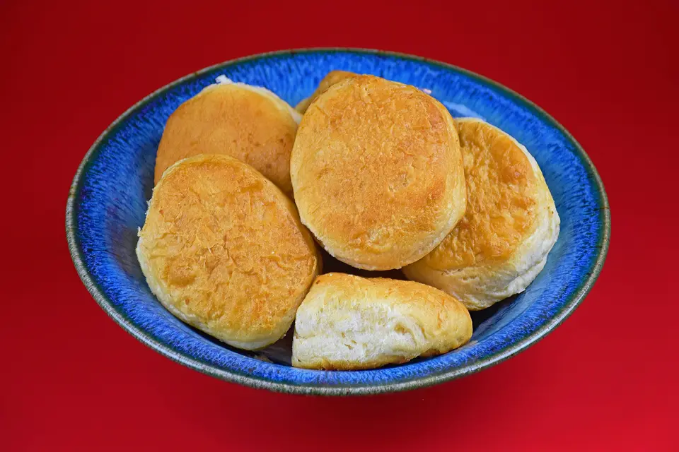 Golden buttermilk biscuits piled in a blue bowl on a red table