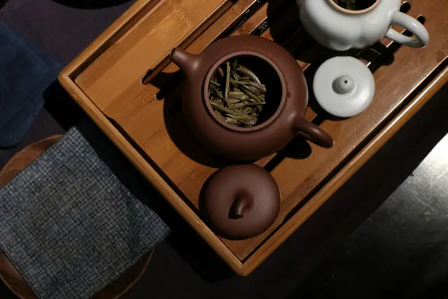 Clay teapot with loose leaf tea on a wooden tea tray beside small cups