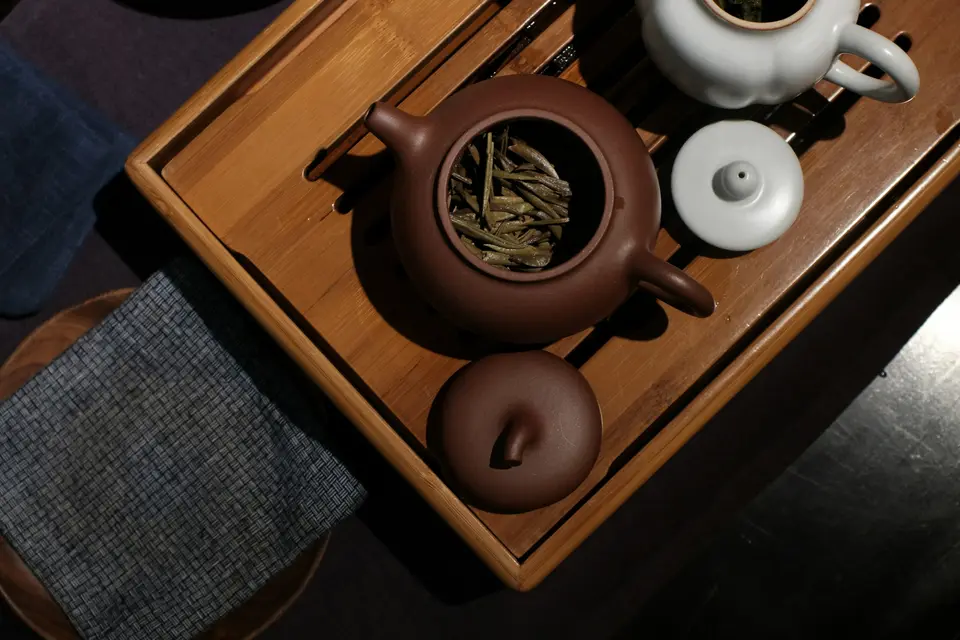 Clay teapot with loose leaf tea on a wooden tea tray beside small cups