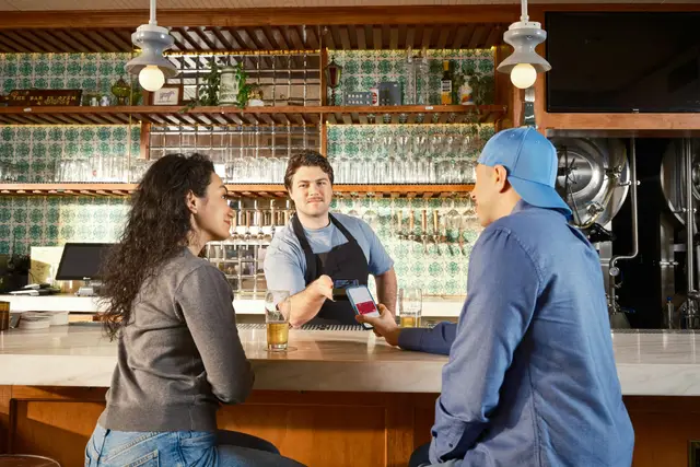Bartender chatting with two guests across a taproom bar