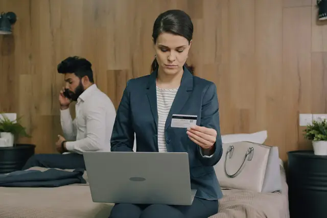 Business woman holding a payment card while completing a transaction on her laptop