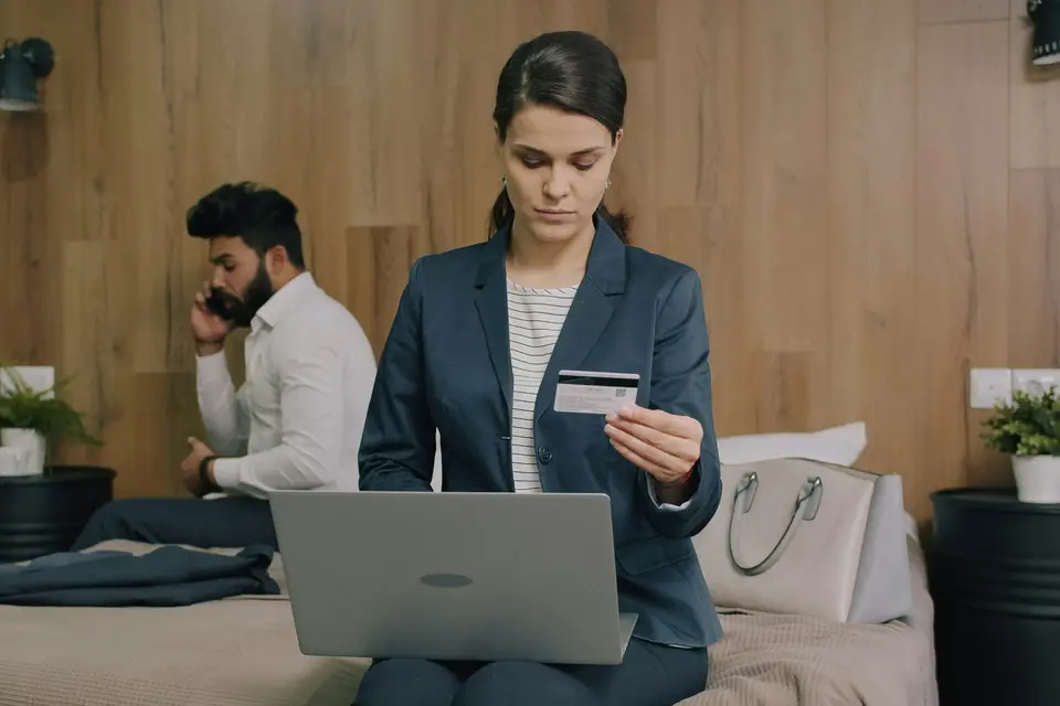 Business woman holding a payment card while completing a transaction on her laptop