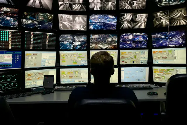 Analyst at a desk facing a large wall of monitoring screens in an operations center