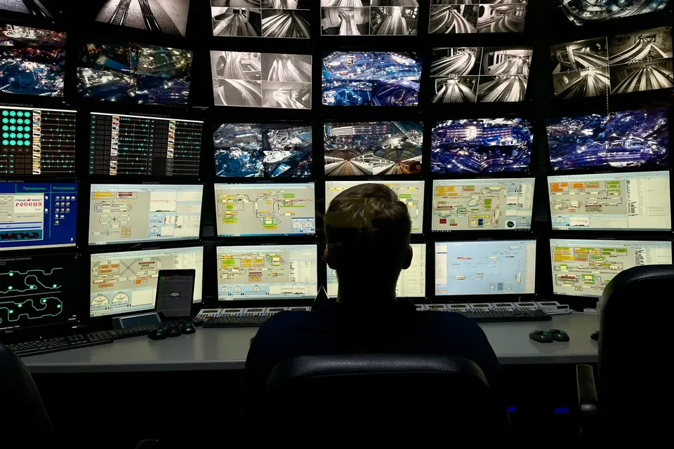 Analyst at a desk facing a large wall of monitoring screens in an operations center