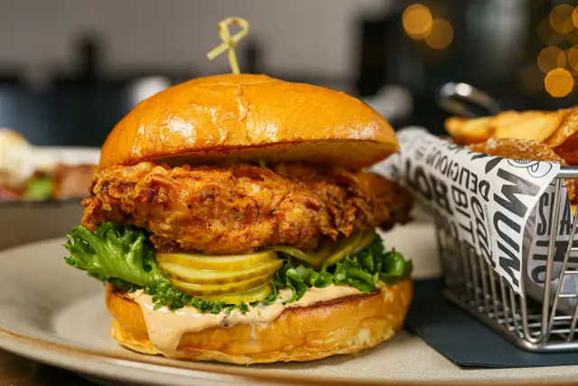 Crispy fried chicken sandwich with pickles on a plate next to fries