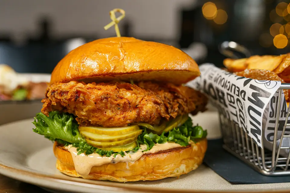 Crispy fried chicken sandwich with pickles on a plate next to fries