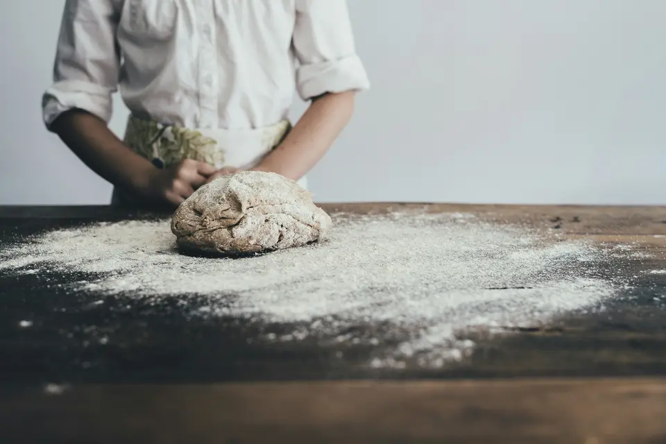 Hands kneading bread dough on a floured wooden table