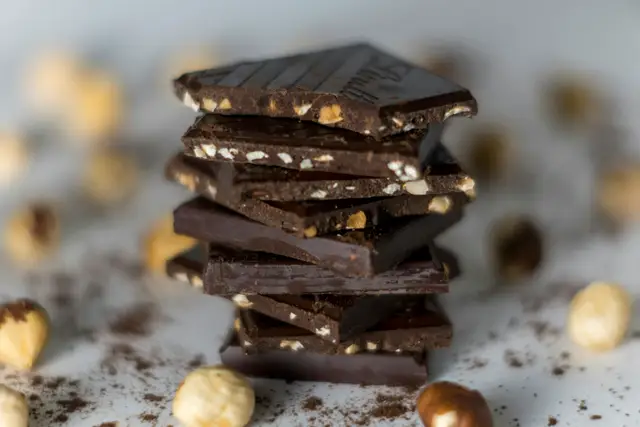 Stack of broken dark chocolate pieces on a dark surface with cocoa crumbs