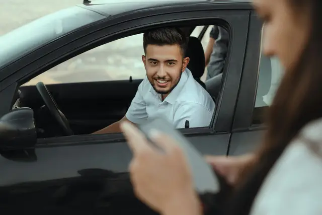 Smiling car buyer in the driver’s seat talking with a salesperson holding a tablet beside the car