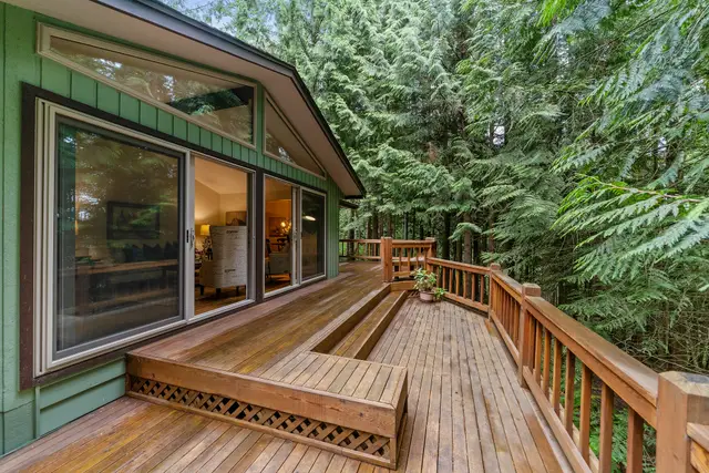 Wooden deck with built-in steps and railings wrapping a home among evergreen trees