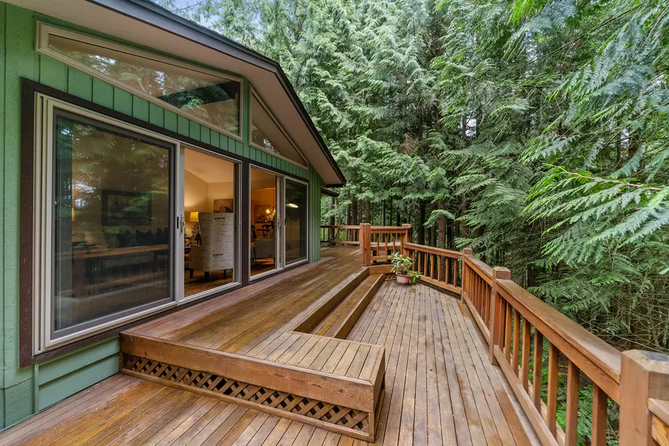 Wooden deck with built-in steps and railings wrapping a home among evergreen trees