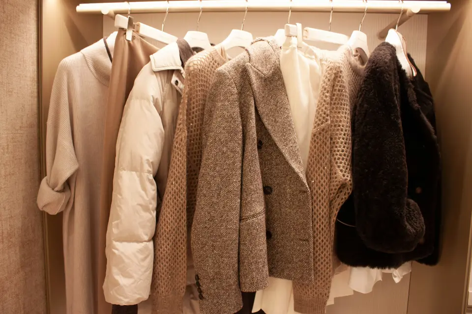 Coats and knitwear in soft neutral tones hanging on a closet rail