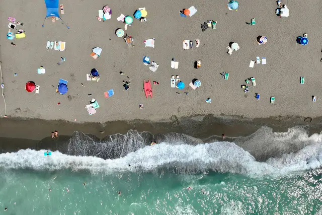 Aerial view of a sandy beach dotted with colourful umbrellas and sunbathers beside the surf