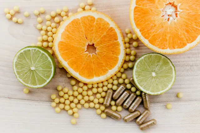 Halved oranges and limes with small yellow softgels and brown capsules scattered on a light wooden table