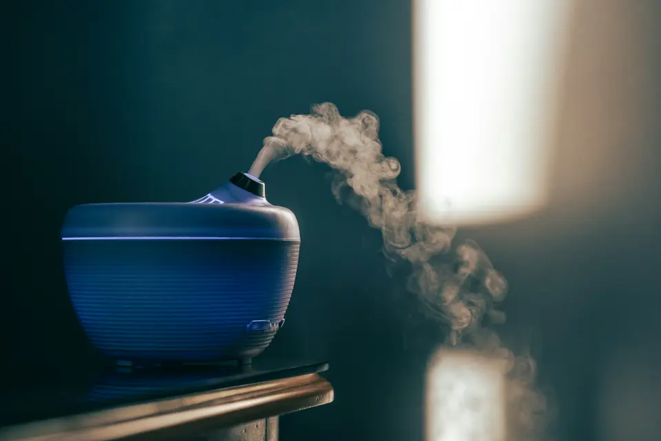 Blue aromatherapy diffuser releasing mist in a dim room