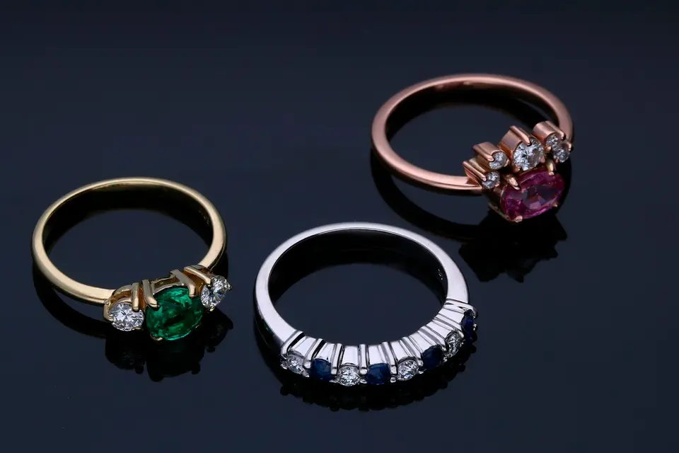 Three gemstone rings in silver, gold and rose gold on a dark background