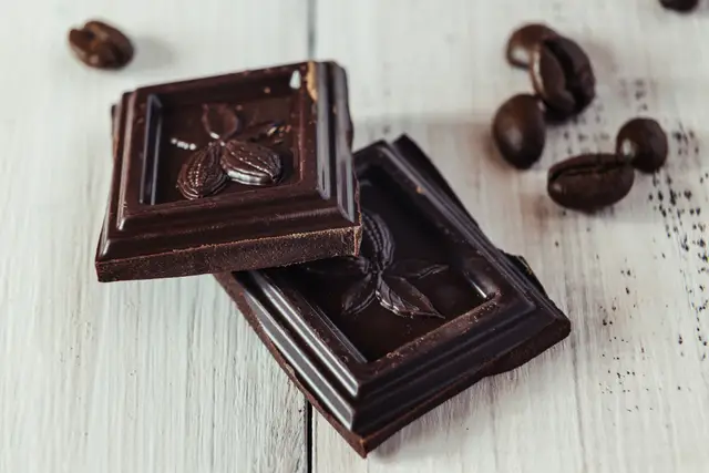 Squares of dark chocolate with cacao beans on a white wooden table