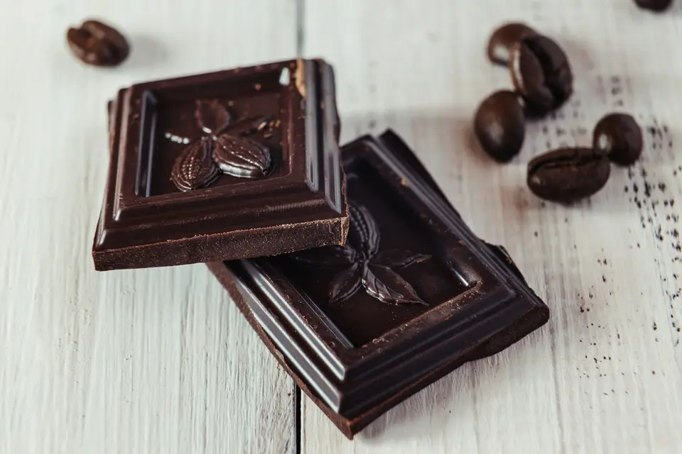 Squares of dark chocolate with cacao beans on a white wooden table