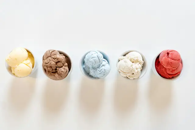 Five small bowls of ice cream in different flavors lined up on a white table