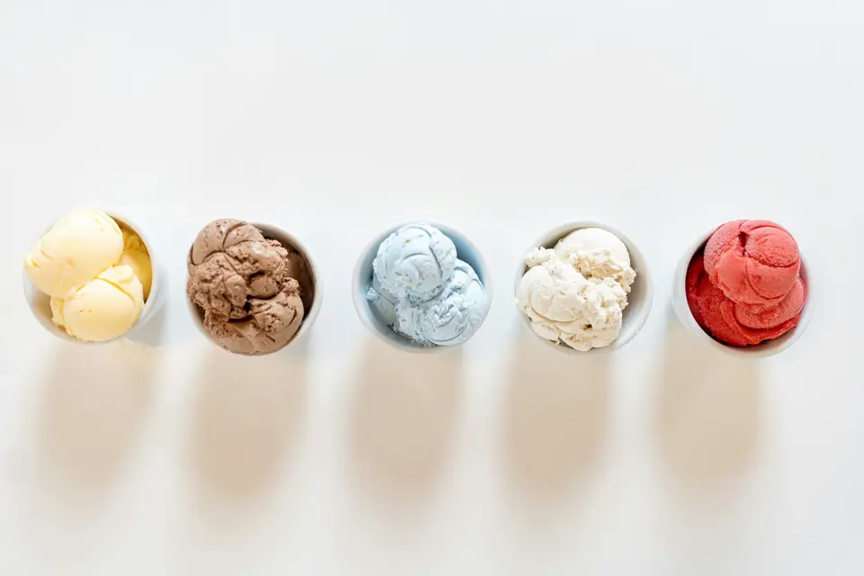 Five small bowls of ice cream in different flavors lined up on a white table