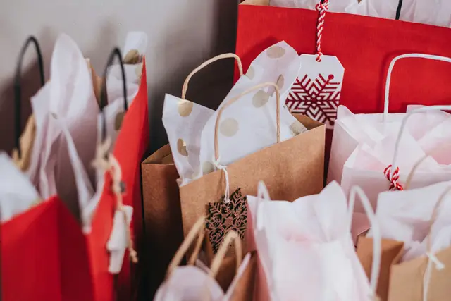 Red, white and brown paper shopping bags filled with tissue paper and holiday gift tags