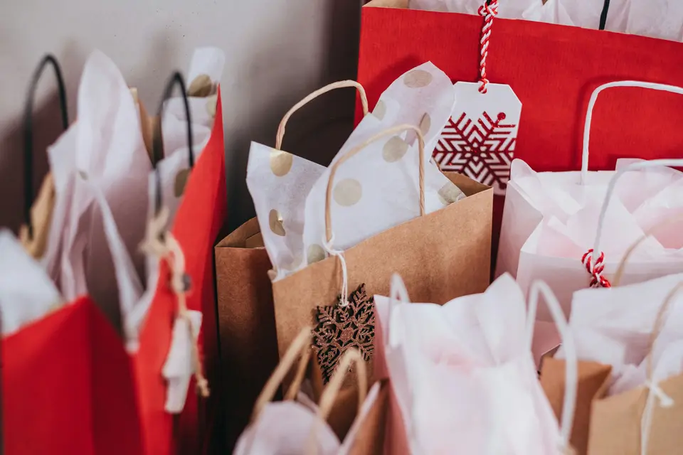 Red, white and brown paper shopping bags filled with tissue paper and holiday gift tags