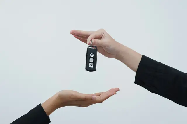 One hand passing a car key to another, the moment a car sale closes