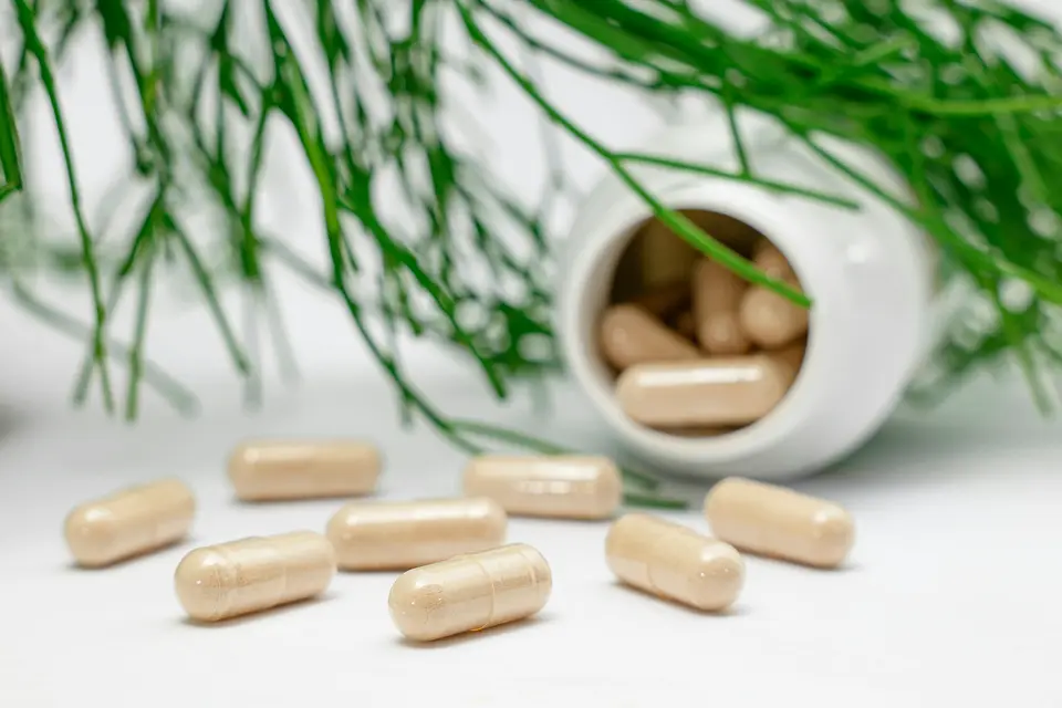 Beige capsules spilling from a white bottle beside sprigs of green pine