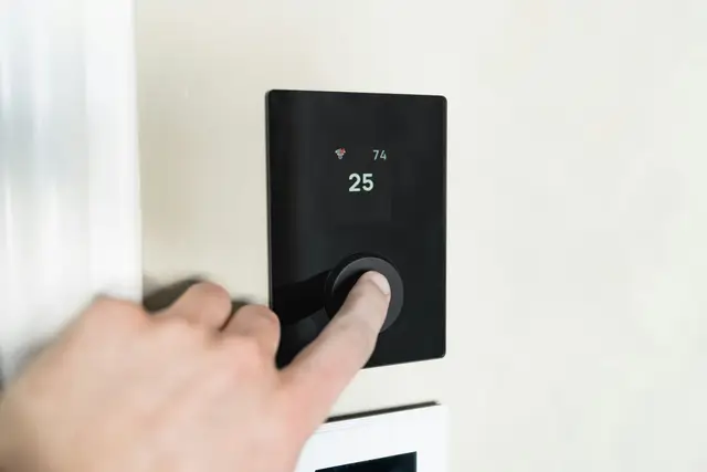 Hand pressing the dial of a modern wall thermostat in a bright home