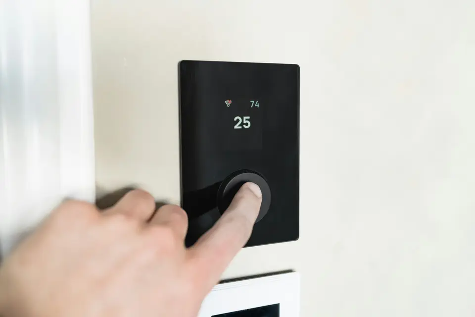 Hand pressing the dial of a modern wall thermostat in a bright home
