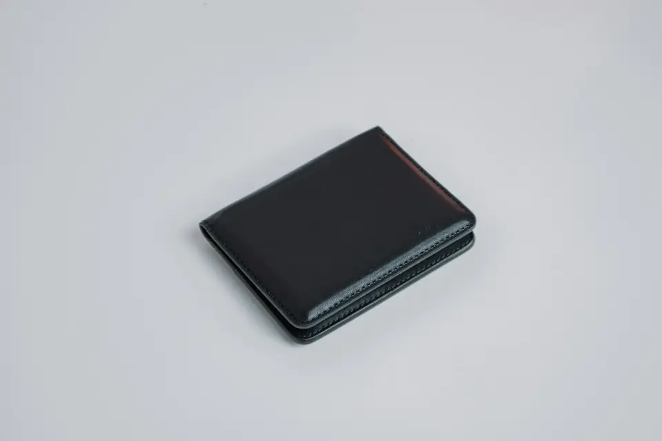 Slim black leather card wallet on a plain light grey surface