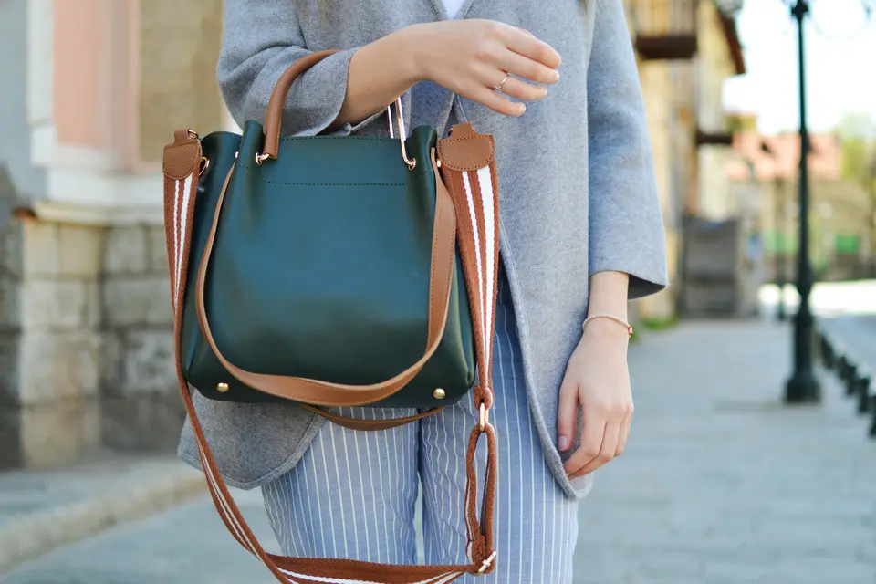 Woman on a city sidewalk carrying a green leather handbag with a tan strap