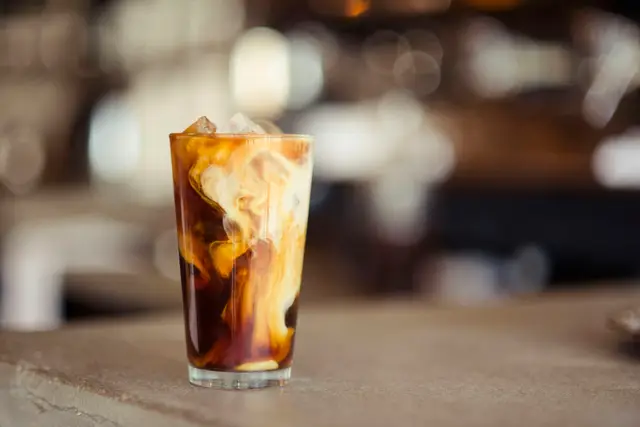 Iced coffee with cream swirling in the glass on a kitchen counter in morning light