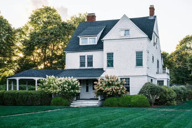 Well-kept white house with a dark roof, blue hydrangeas and a freshly mown lawn
